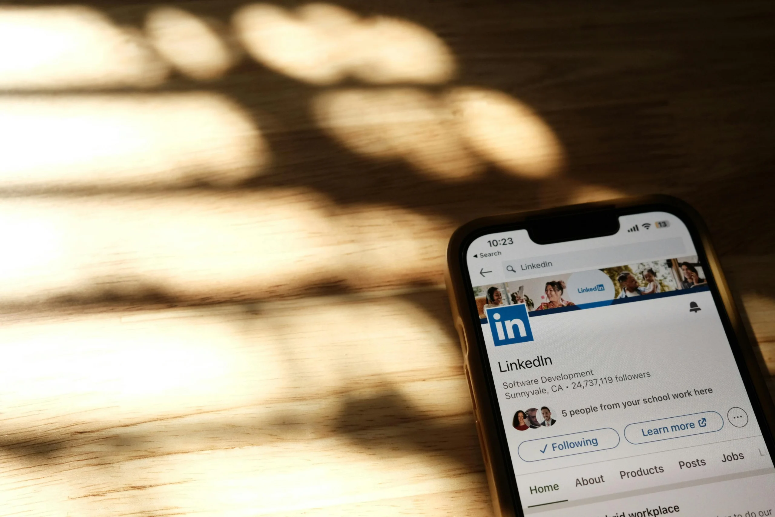 Smartphone ligt op houten tafel met open LinkedIn-pagina, toont volgers, locatie en tijd 10:23