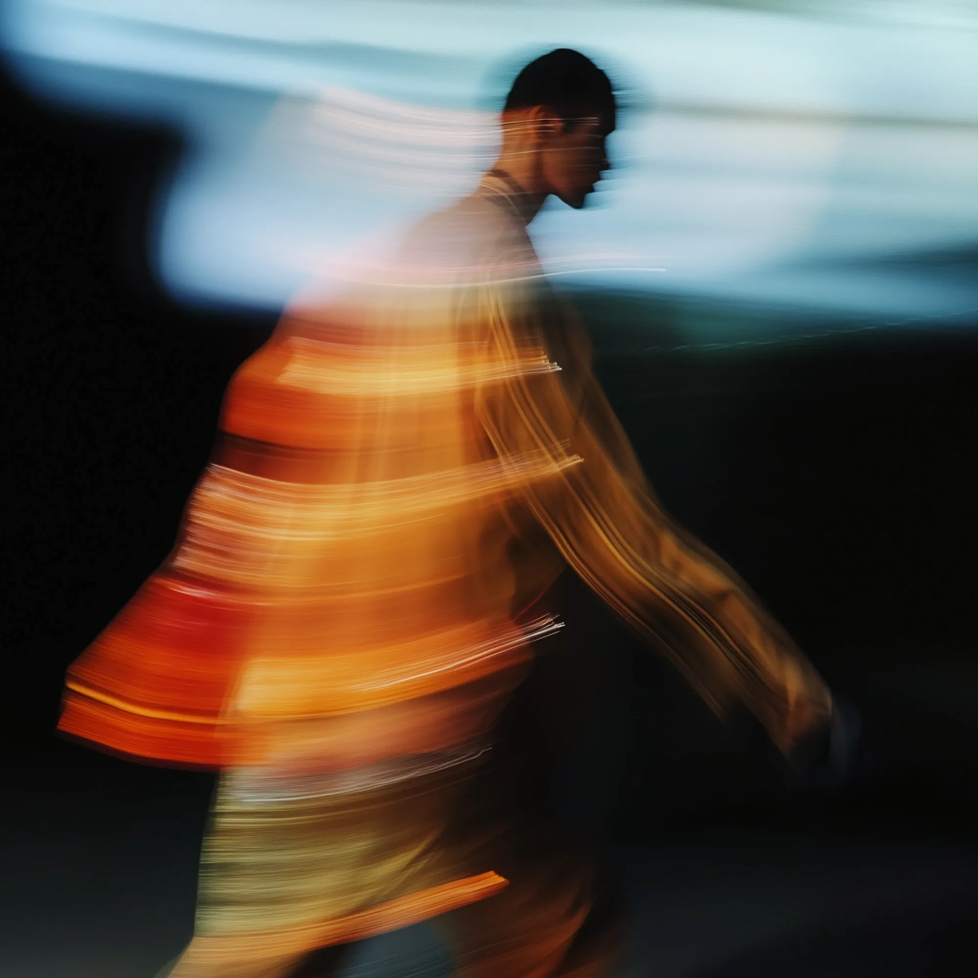 Onscherp portret van bewegend persoon met oranje en gele strepen tegen donkere achtergrond